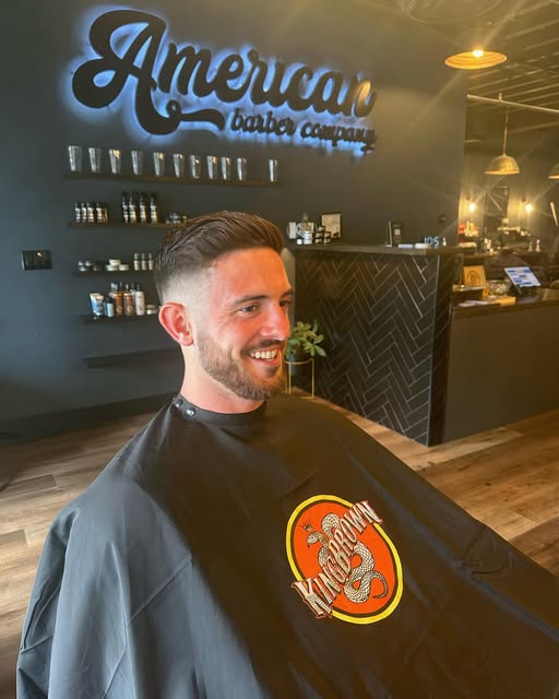 Client with a fresh taper fade and side part in the chair at American Barber Co
